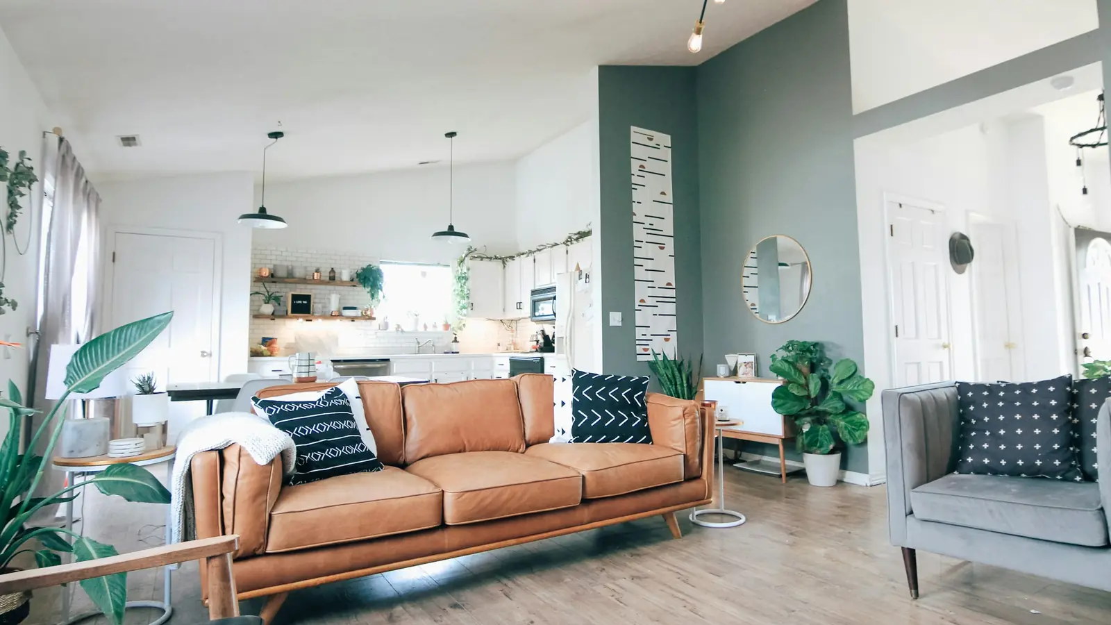 Lichte woonkamer met cognackleurige bank, planten en een open keuken